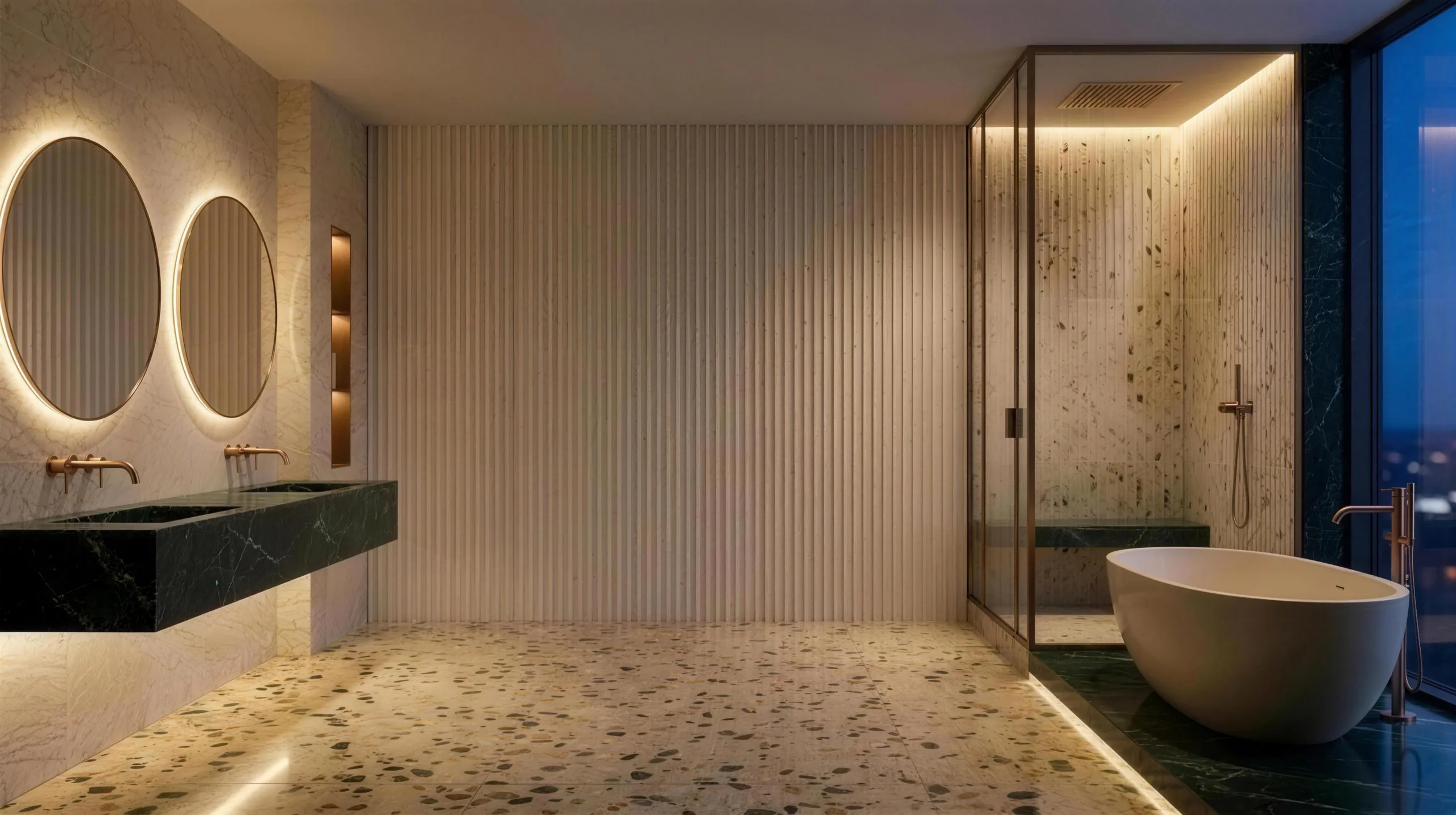 A softly lit bathroom finished in cream marble, fluted stone, green marble and terrazzo, with bronze fittings and a city view at dusk.