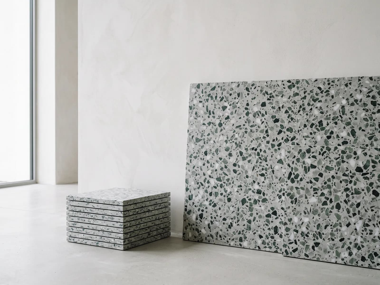 Stack of terrazzo tiles beside a large terrazzo slab against a wall