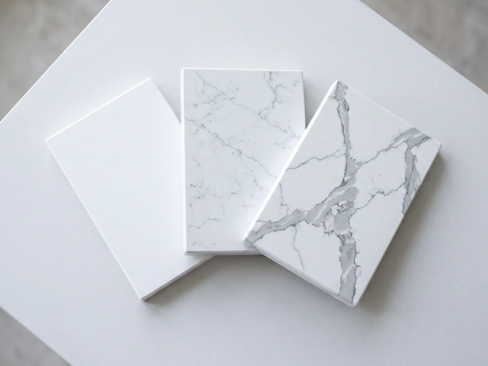 Three white quartz samples fanned: plain, Carrara-look and Calacatta-look