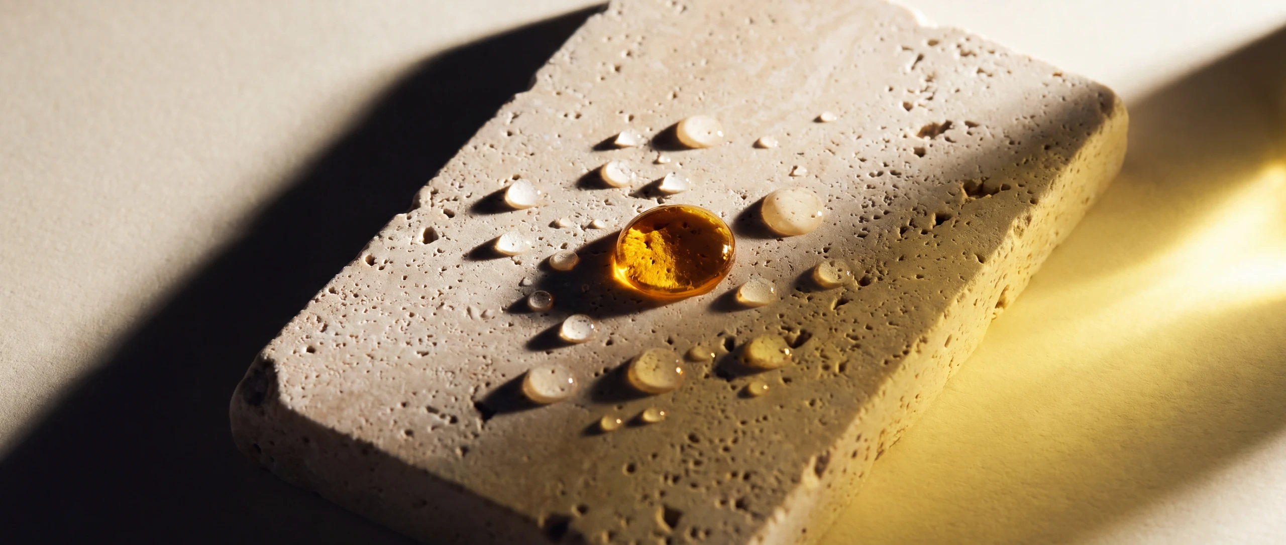 Water beads and one amber oil bead standing on sealed honed travertine