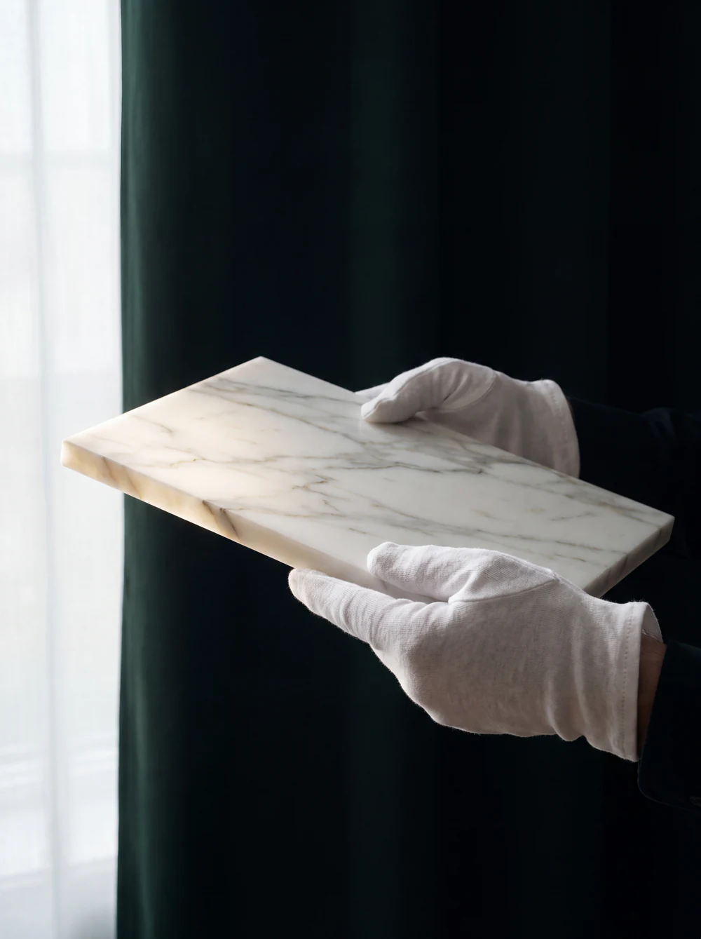 White-gloved hands holding a veined marble sample against the light